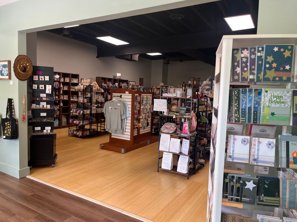 View from the front room of the shop where the spinning card racks are into the rest of the shop.  The image shows one spinning rack on the right, and then many shelves and displays with a variety of merchandise in the background.  