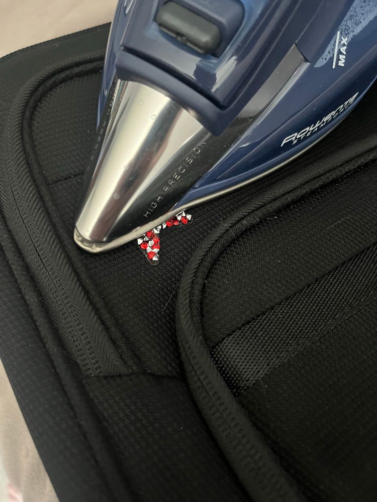 The upper right corner of a black suitcase, with the front tip of a household laundry iron in the top third of the image, with a few red and silver rhinestones peeking out from under it. 