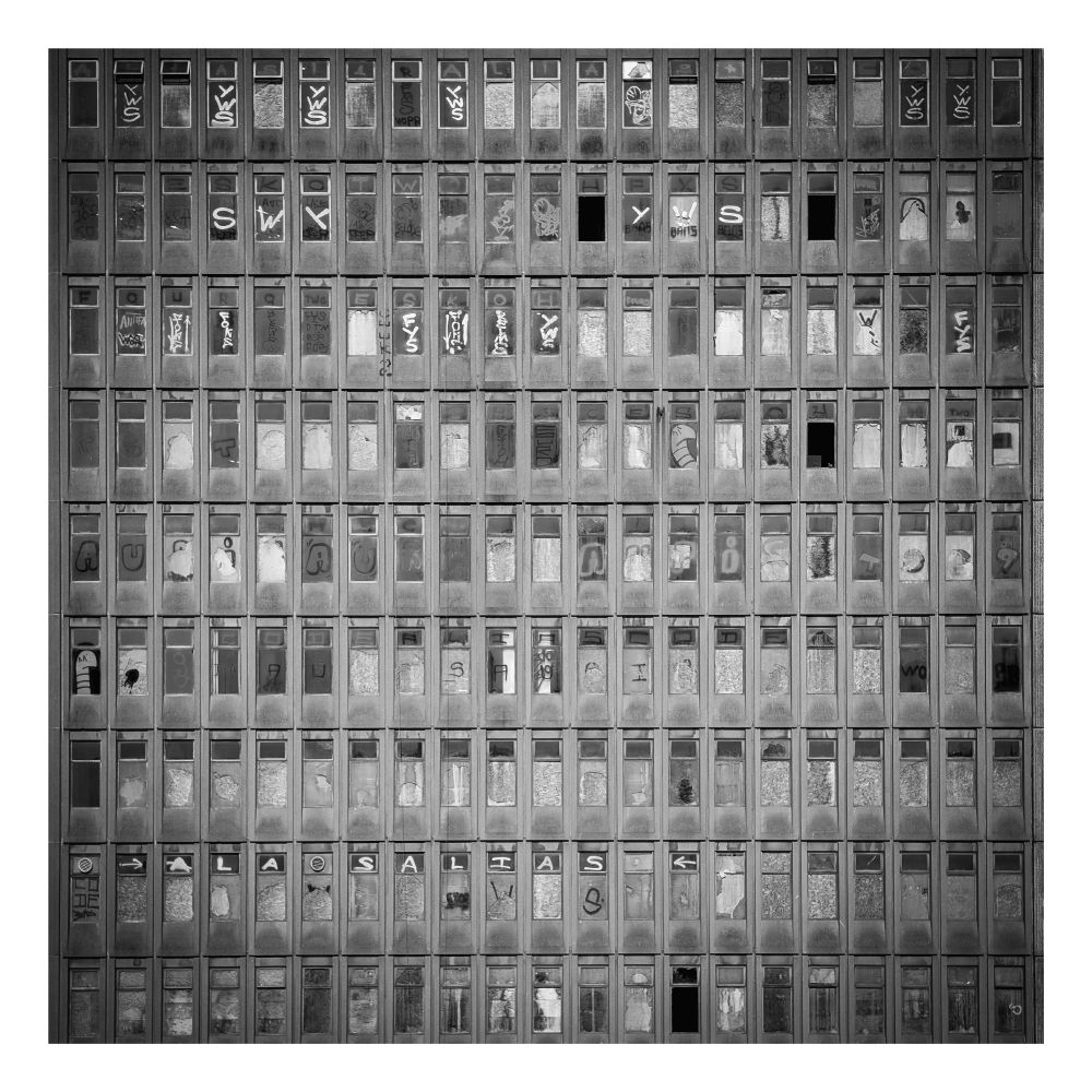A black and white photo of an old abandoned building facade with lots of broken windows and graffiti.