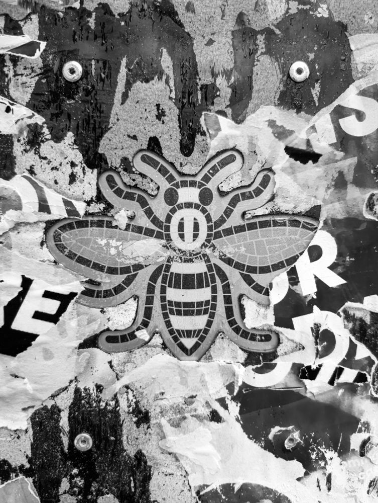 A black and white photo of the Manchester bee logo surrounded by worn street art paste-ups.