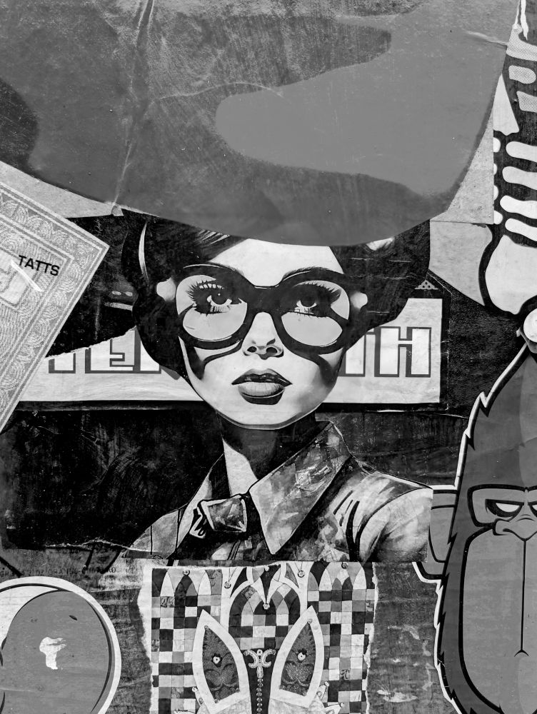 A black and white photo of a collage of street art paste ups with a lady wearing glasses in the centre.