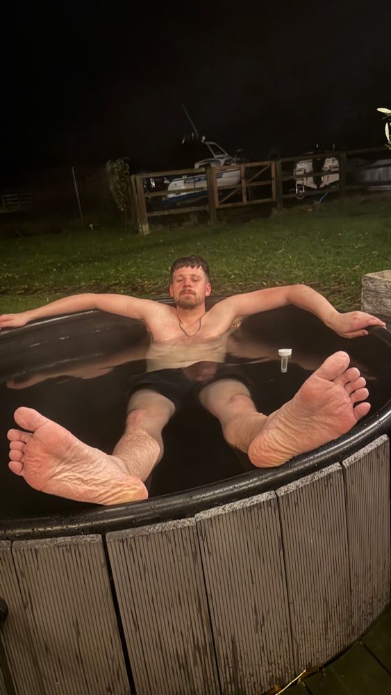 a picture of Danny in a wood fire hot tub, with his feet up on the tub’s edge