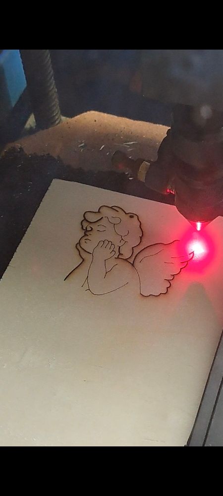 A piece of wood and a red laser carving the image of an small angel into it.