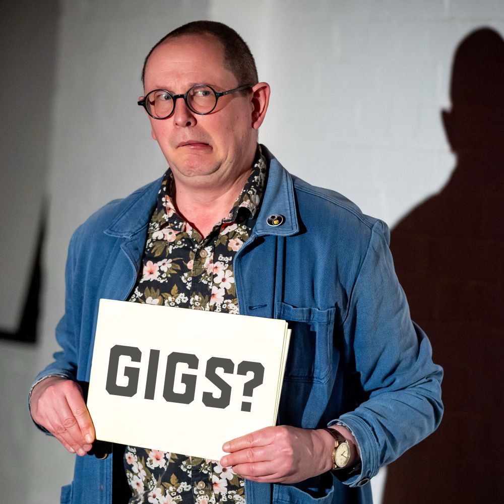 Me looking discombobulated on stage holding a sign saying “GIGS?”.
