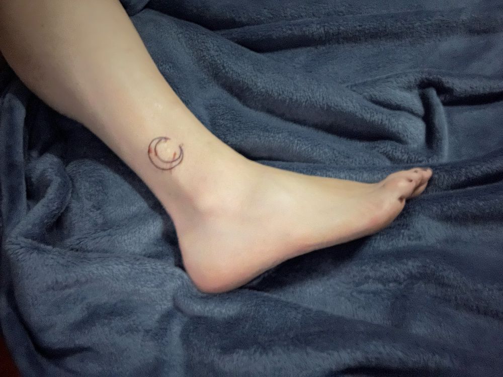 A photo of a leg and foot with a crescent moon tattooed above the ankle. 
