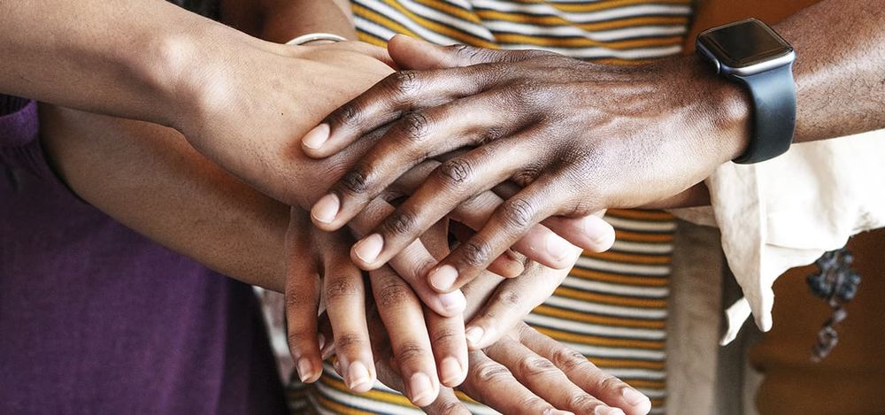 Photograph of several people overlaying their hands in solidarity. I use this photo in the accompanying essay's section on "getting into community" as a great way to keep our spirits up, reenergize, and move forward—together!