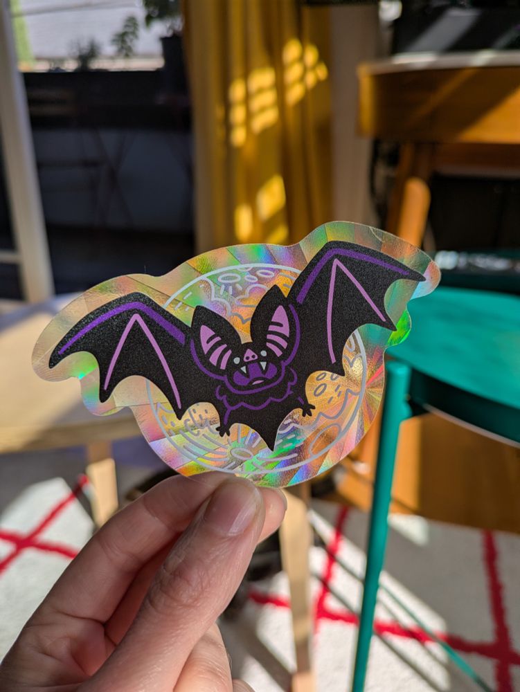 A sparkly transparent sun catcher sticker with a design of a bat over the moon.
