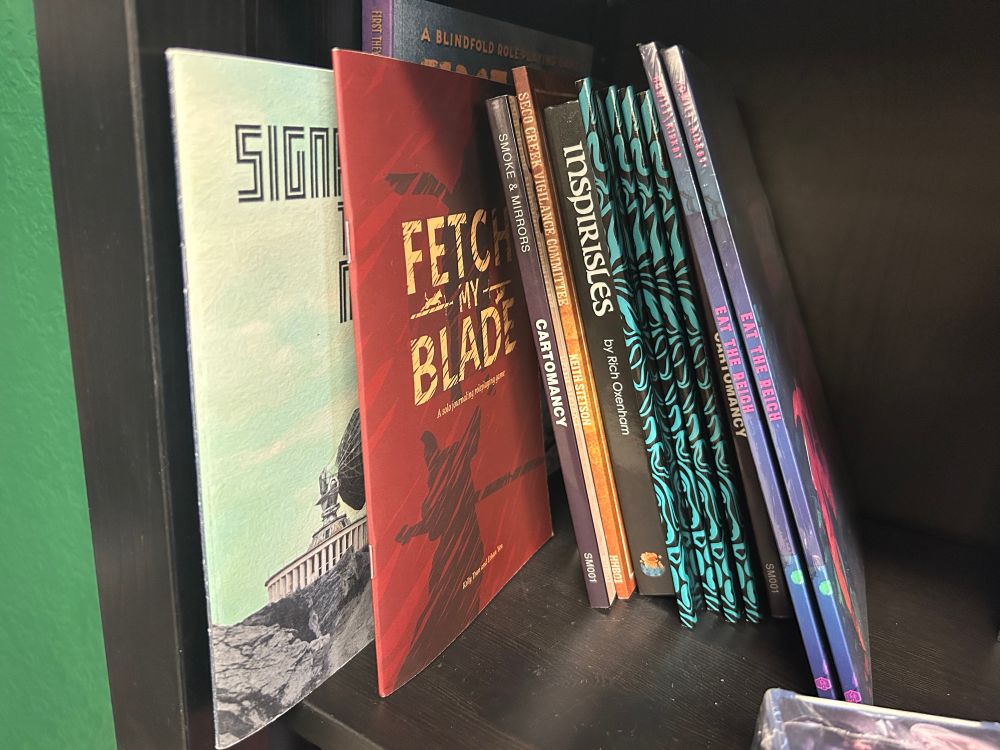 Bookshelf of RPGs which include Signal to Noise, Fetch My Blade, Inspirisles and Eat the Reich