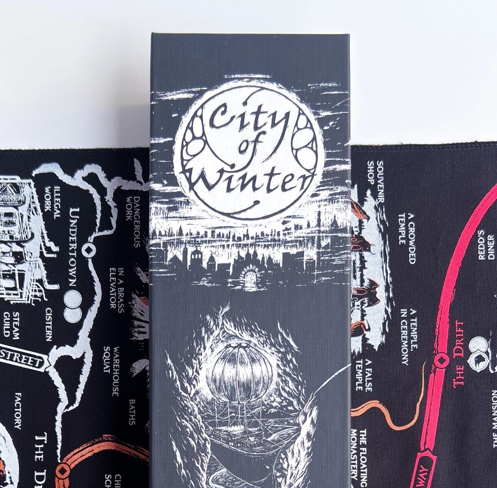 Close up of City of Winter box on the scroll as a background - black and white logo on a detailed darkly inked image of a town and an airship.