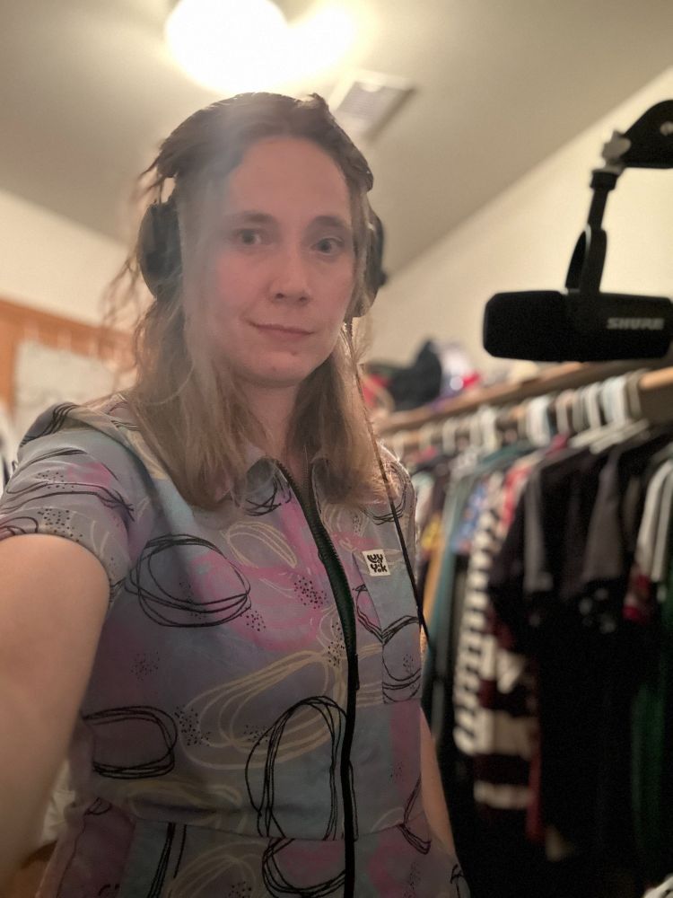 Fiona, a white woman wearing a purple squiggle jumpsuit from Lucy & Yak recording in a clothes closet. 