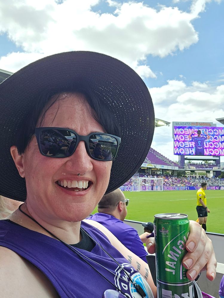 Heather at inter&co stadium, holding a Heineken and wearing a purple Orlando Pride tank top. Behind Heather, the screen shows McCutcheon, the player who scored the goal