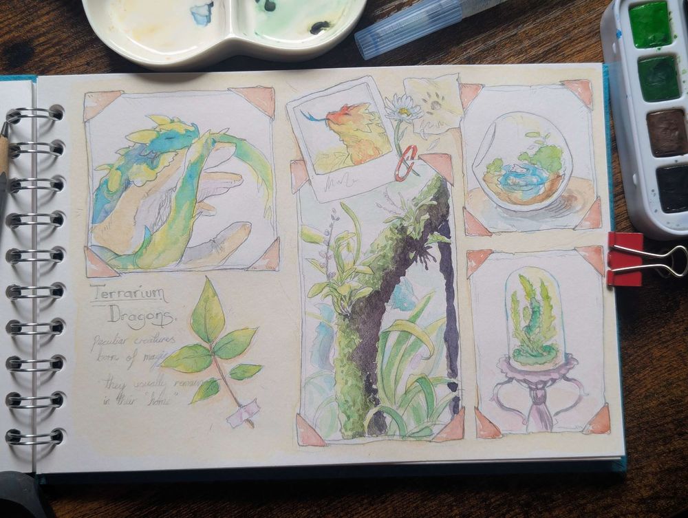 Photo of a sketchbook with tools around it. 
There's a mixture of watercolour sketches that are made to look like a study of animals scrapbook.
images feature my little creatures, called terrarium dragons; small dragons that looks like a cross between a lizard and a mustelid.