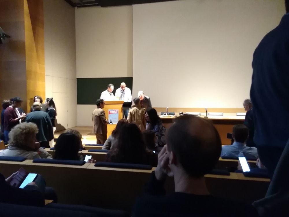 Salle du collège de France, organisateurs en train de discuter, public qui passe