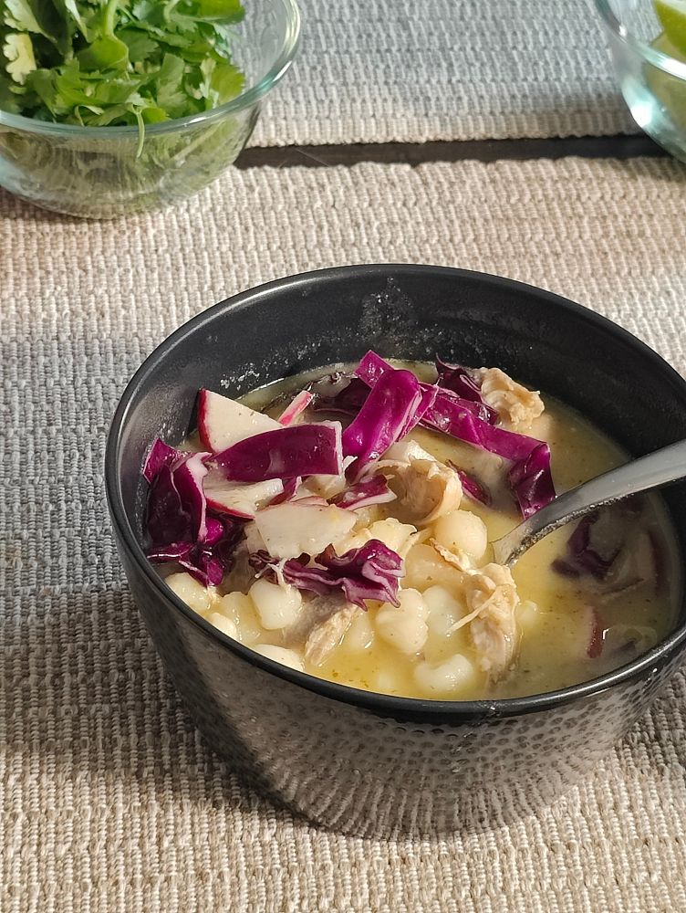 A cute bowl of pozole Verde with red cabbage and radishes on top.