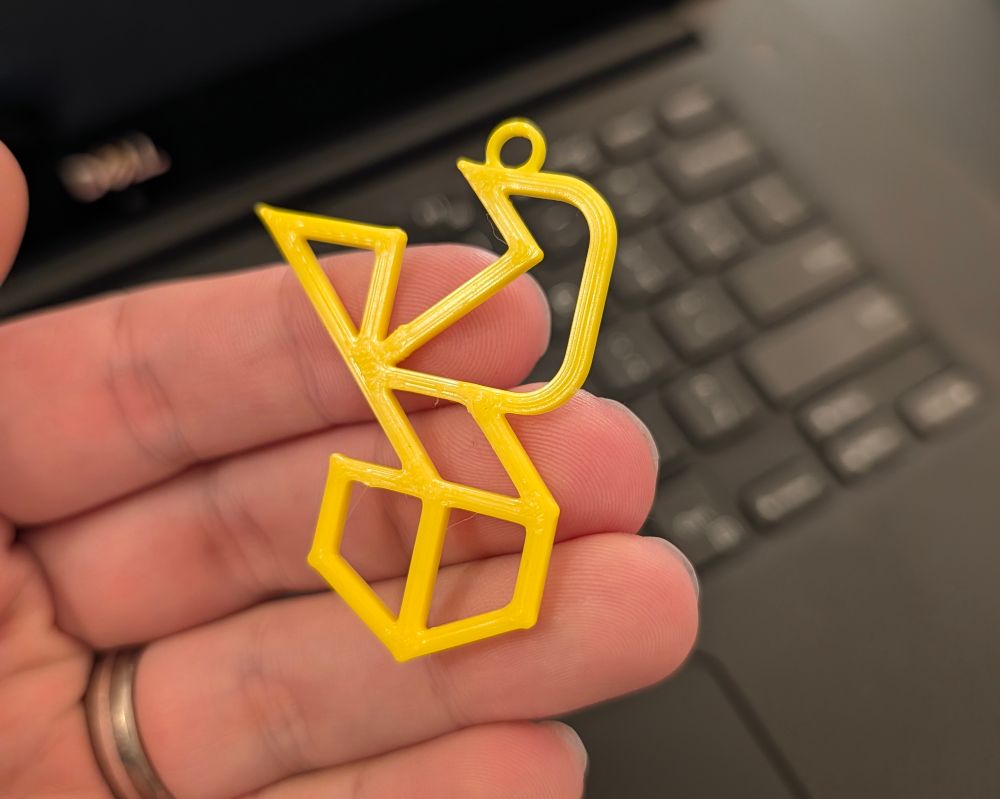 Close-up of a 3D printed ROOST keychain being held. The logo is a geometric line art representation of a bird on a shield-shaped perch.
