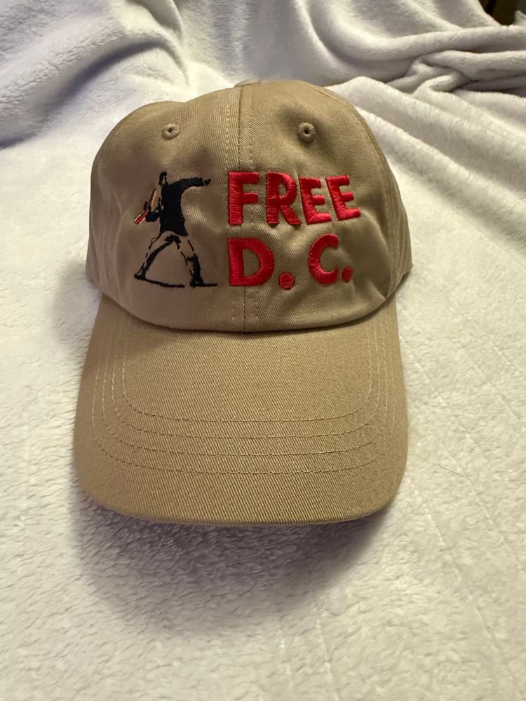 A baseball cap with Free DC embroidered on it and a Banksy-style image of a man throwing a sandwich