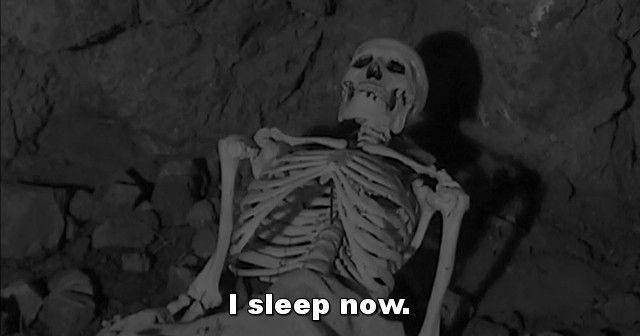 A black and white shot of a skeleton mannequin in a cave, and the subtitle of it saying "I sleep now."