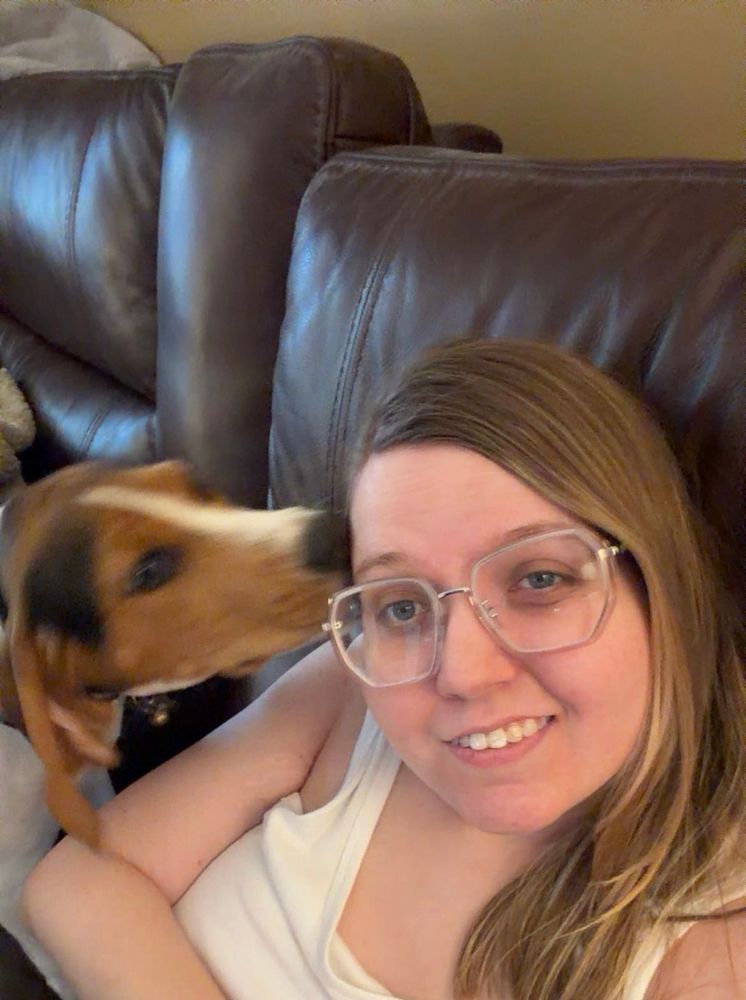 My (brown/black/white) puppy Lucy giving me morning kisses while I smile in pain because she was hurting me and she’s way heavier than she looks