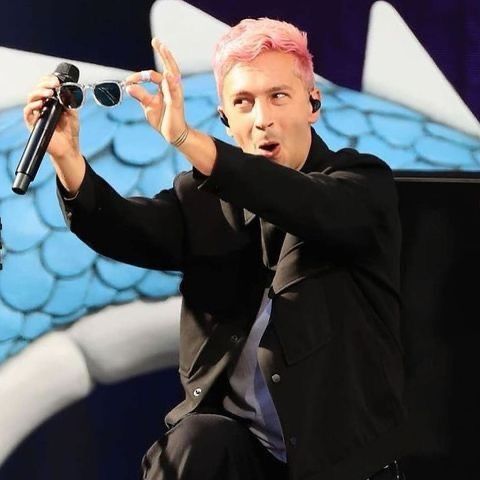 Tyler with pink hair holding sunglasses out to the crowd making a funny face 