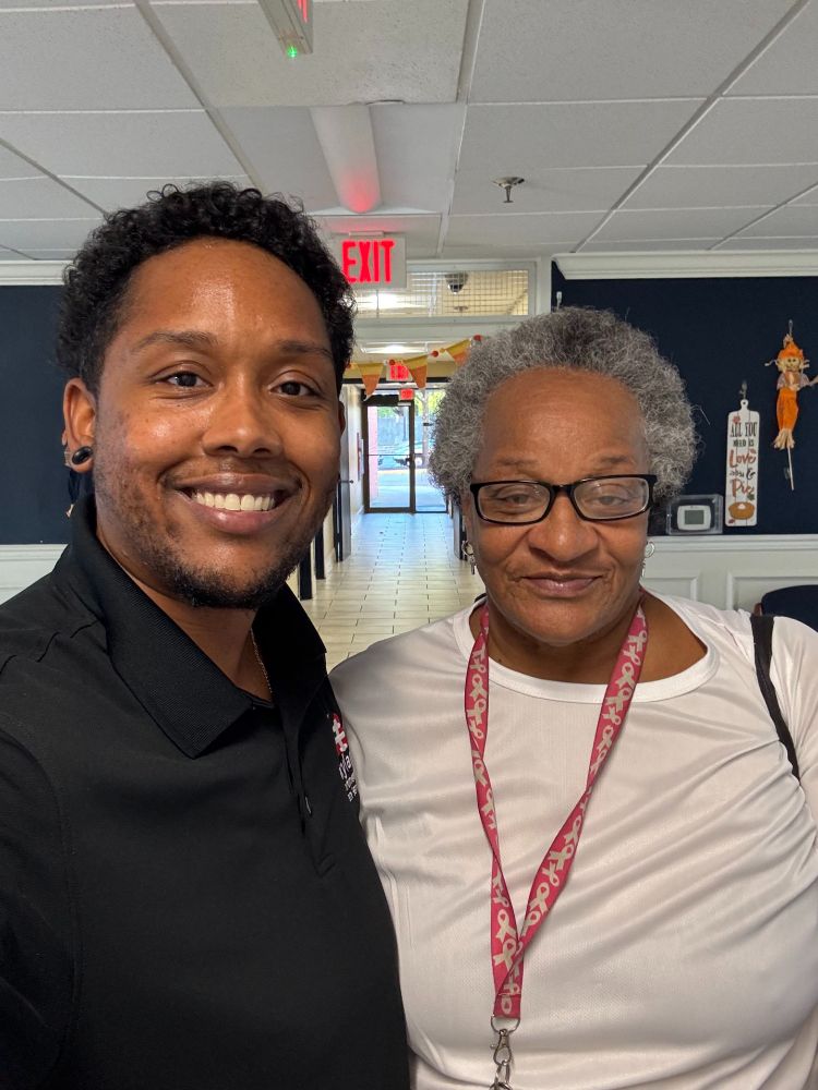 A selfie showing a smiling man and an older woman standing side by side in a hallway.