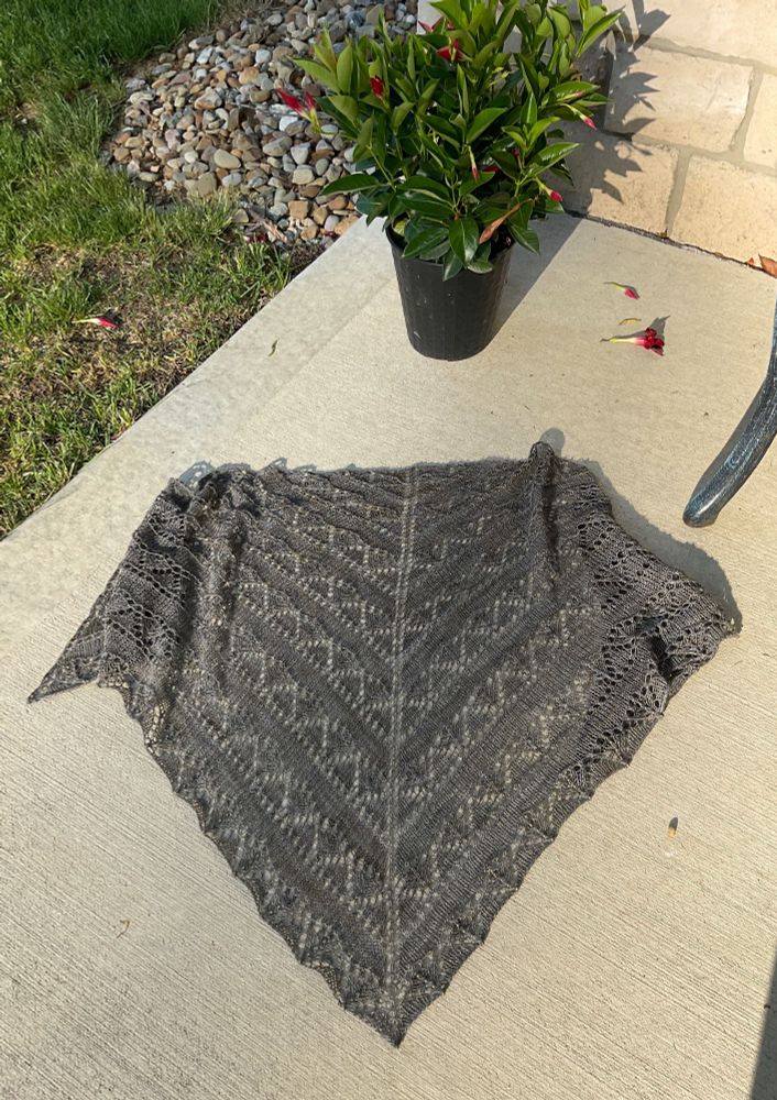 Handknit shawl spread out in the sunshine with a pot of red flowers.