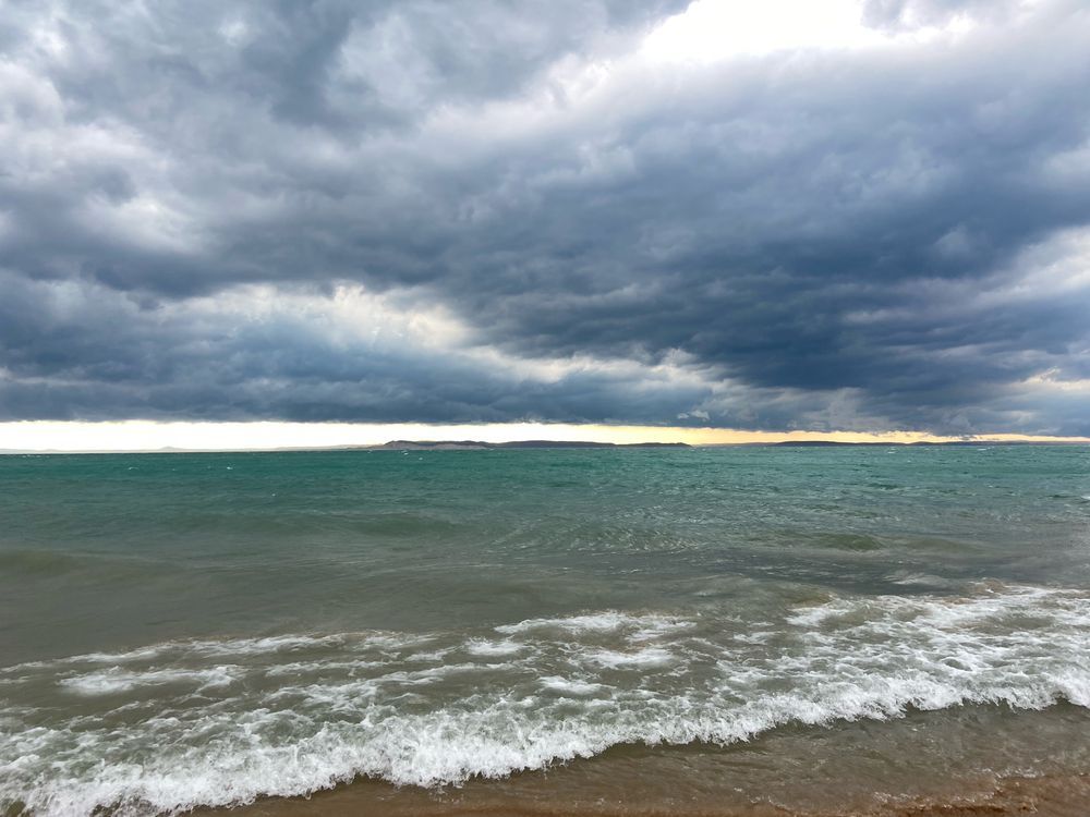 A thunderstorm approaches over rough water. At the horizon, a band of clear sky glows peach. 