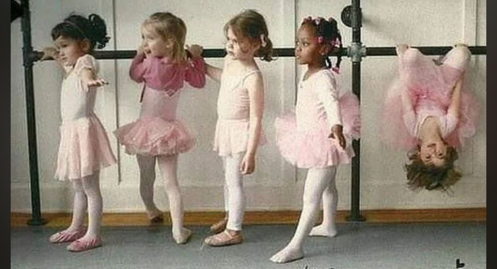 Five little ballerinas, dressed in varying shades of pink leopards and tutus, are lined up in front of a ballet barre, with one ballerina hanging upside down from the barre. 