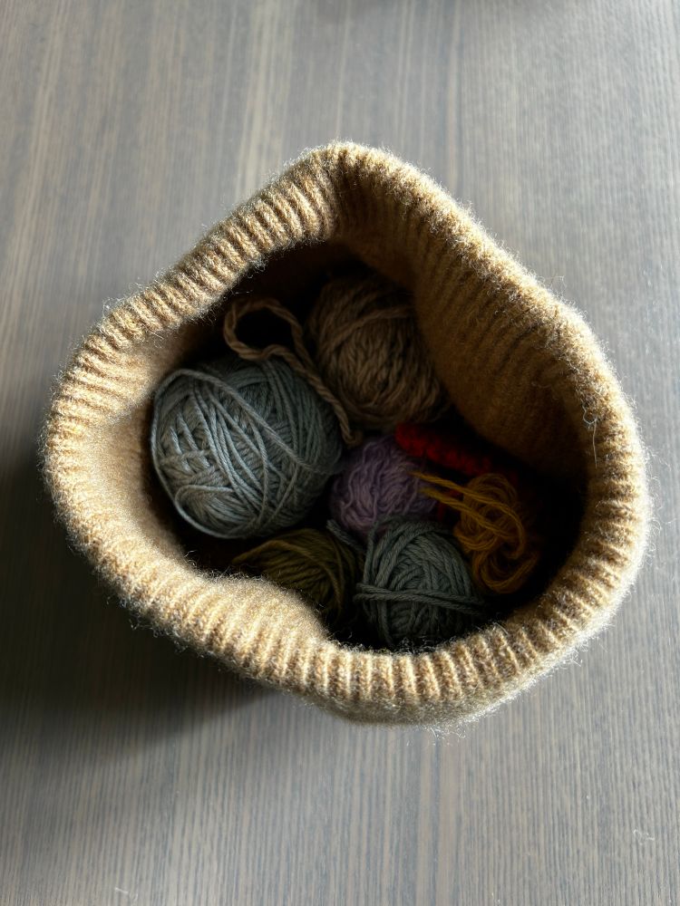 The same felted beanie placed on the desk holding scraps of yarn as if it’s a basket. 