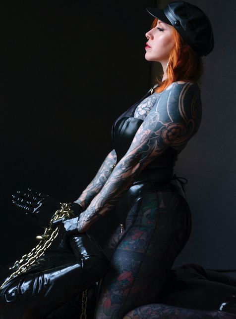A sunlit Chloe Nova straddling a chained and latex bound sub. 