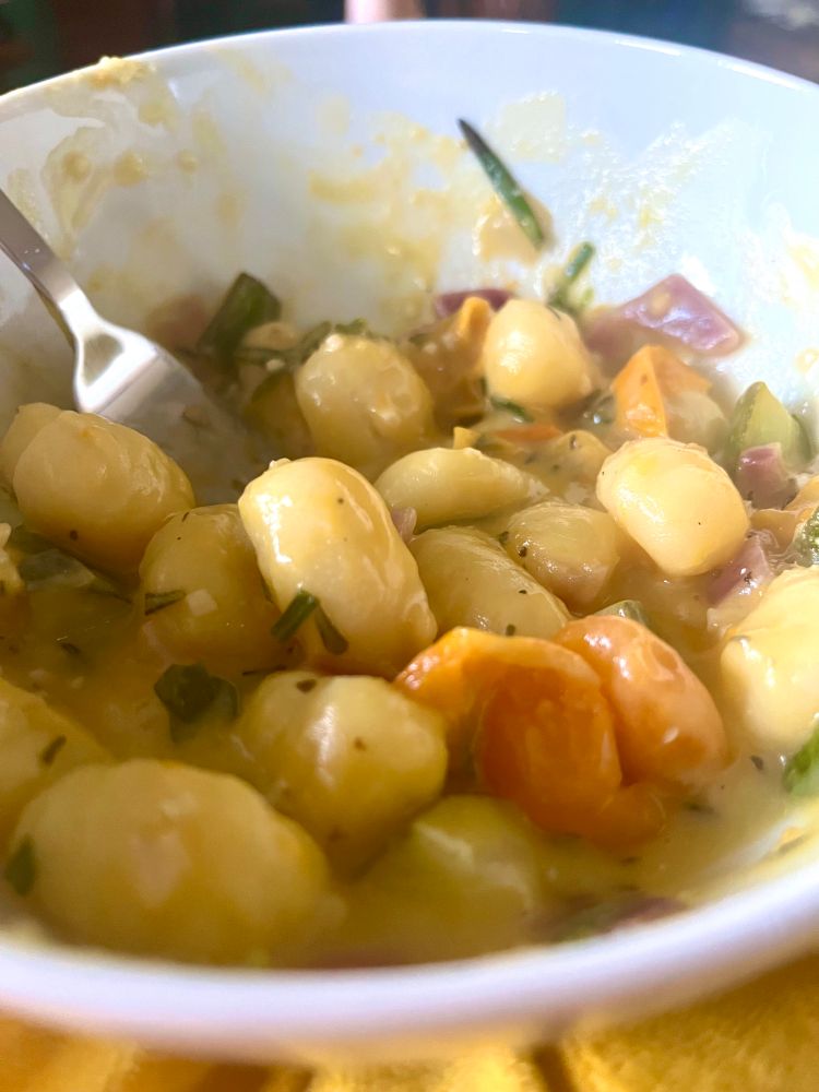 A closeup of a bowl of gnocchi. It is saucy and herby and there are burst cherry tomatoes in it. 