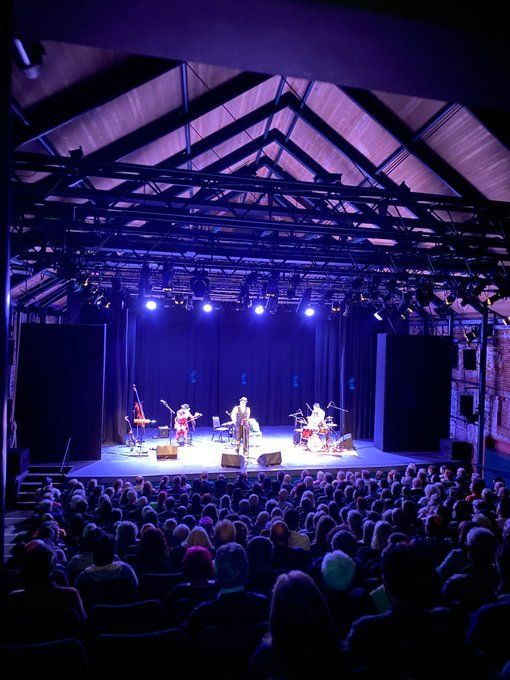 Norwich Playhouse, a midscale theatre with a raftered ceiling. Lit in blue and purple, a band on the stage