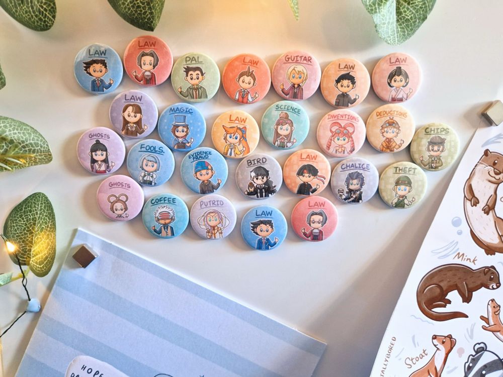 A photo of a magnet board with a collection of round magnets with Ace Attorney characters drawn in a kawaii style. Other things stuck to the board are leaf-style fairy lights, a greetings card, and a mustelid sticker sheet.