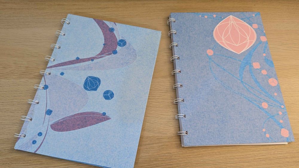 Two notebooks I made, each with a sort of swooshy design, and a bunch of little stylized dice, inspired by the art style called "The Glasgow School".