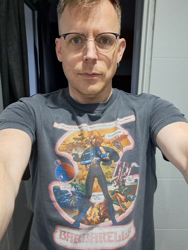 A selfie of we wearing a tshirt that was once black but is now very faded and grey. It has a very large print of Barbarella on the front.