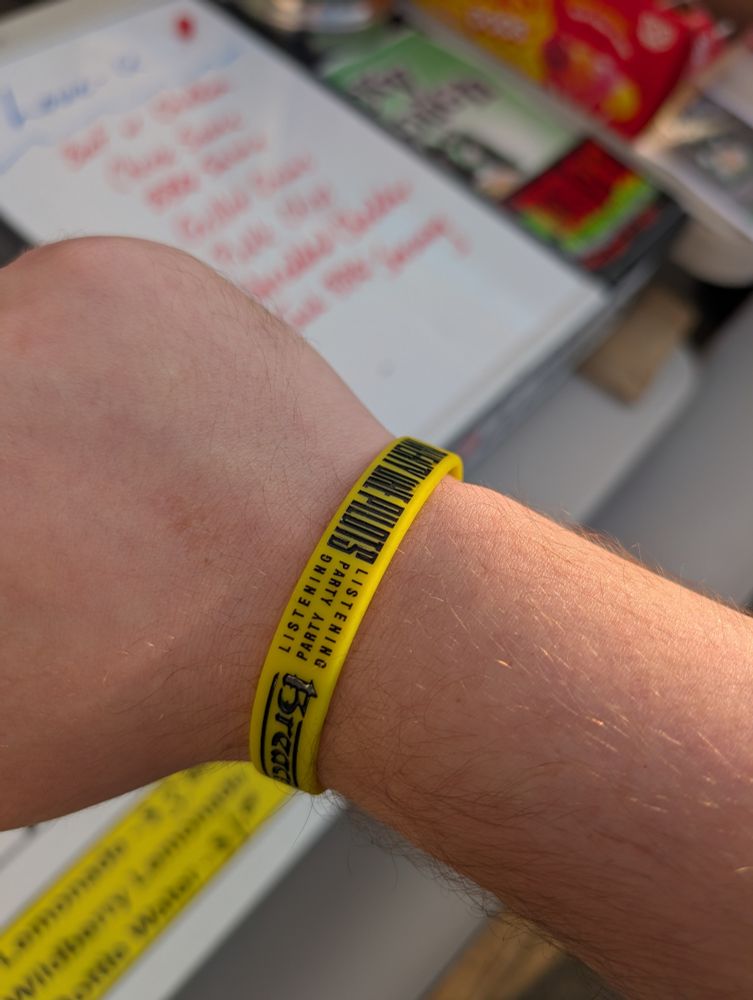 My arm with a yellow rubber wristband printed with the phrases "Twenty One Pilots", "Album Listening Party", and "Breach".