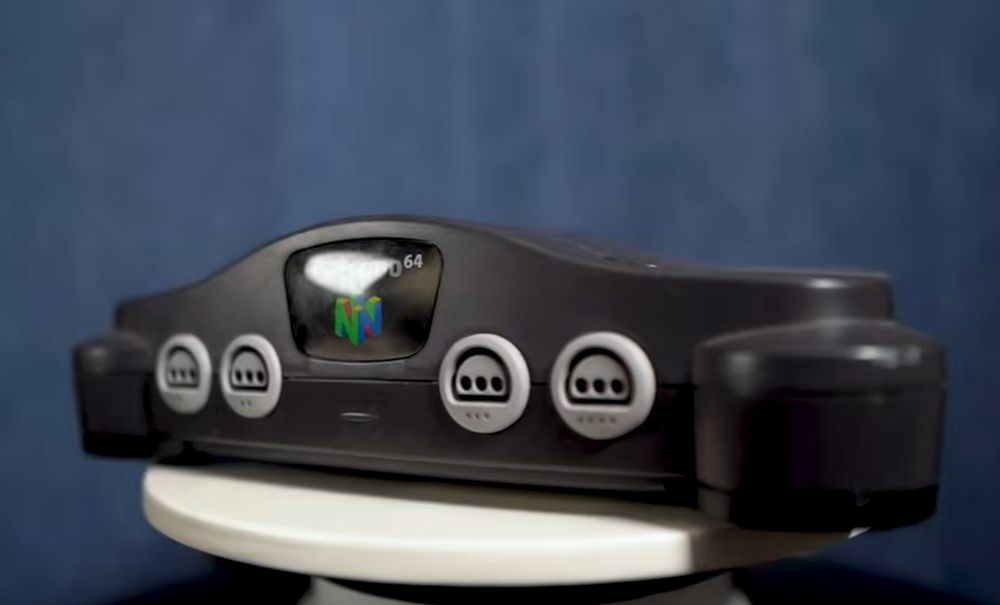 A screenshot from the video "I Calculated the OBJECTIVELY BEST Nintendo Console" by the youtuber JWittz, featuring a Nintendo 64 console upon a podium against a blue backdrop