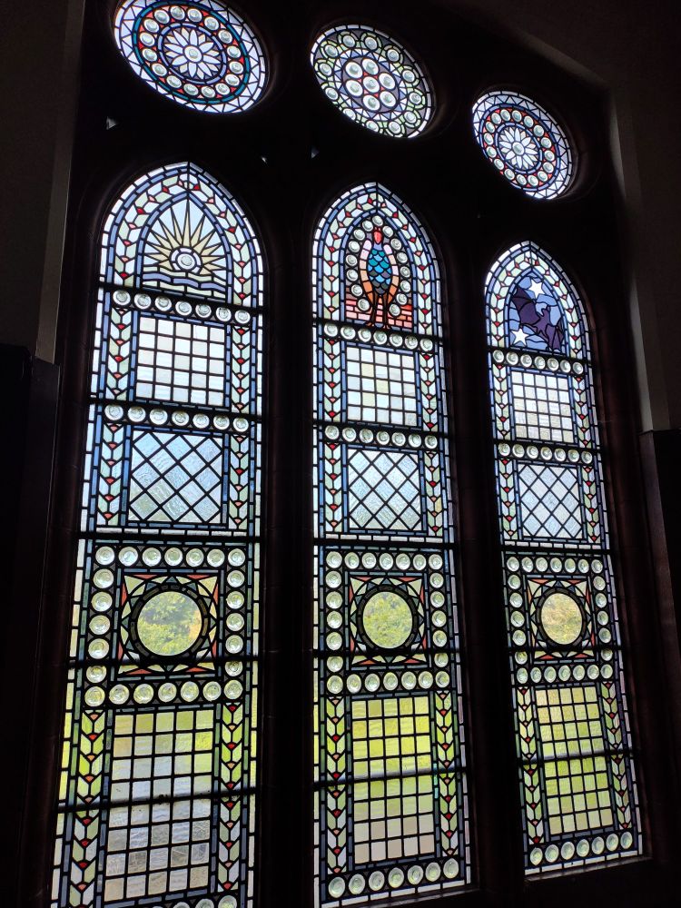 Stained glass window containing representations of a colourful bird and a bat against the night sky with two stars