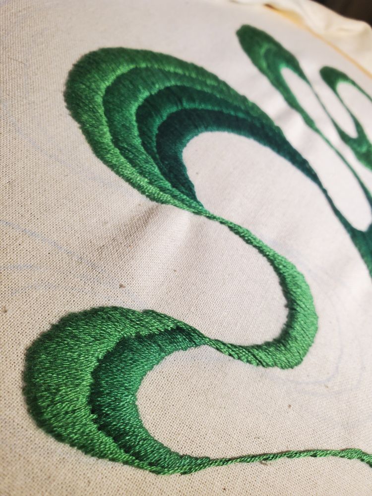 A close up of green satin stitching in a curvey abstract pattern.