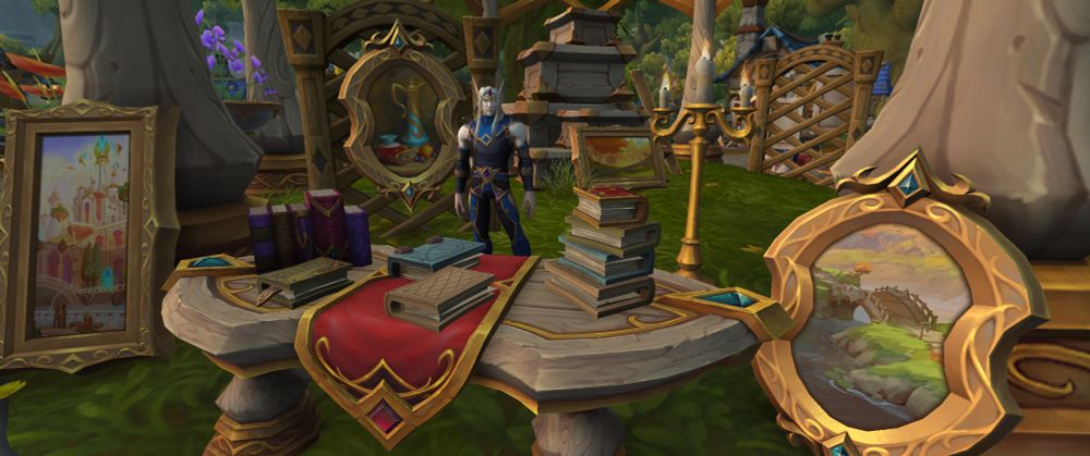 Screenshot of an artist standing with his wares, several gold framed painints, and books that are stacked on a table that sits at the front.
