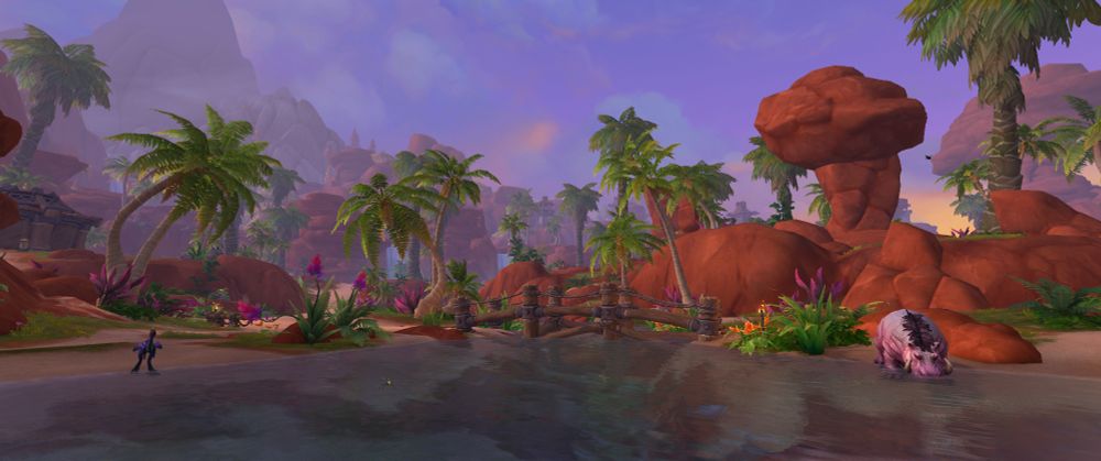 Screenshot from WoW, showing off one section of the Horde Neighborhood. A hippo drinks from the river, palm trees, waterfalls, and red rock formations are in the distance.
