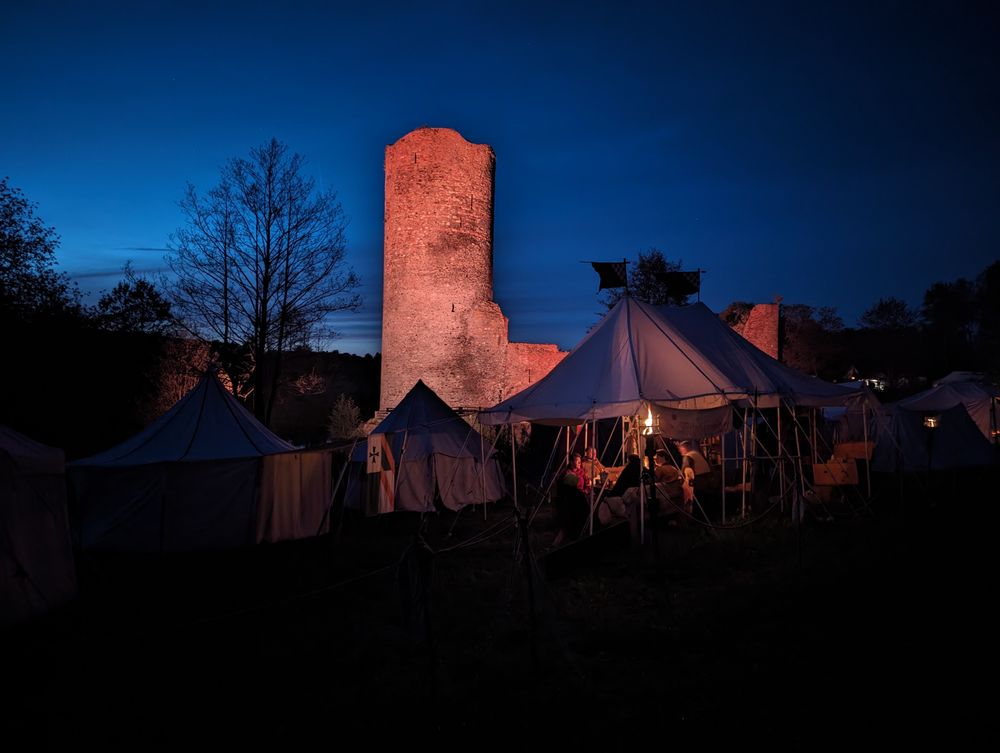 a photo of an old castle with medieval camps at front at night. lights make the castle look brighter