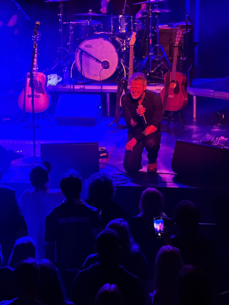 Tom on stage at Folken, Stavanger. He is sitting on the floor, and sings in his microphone. Intense look on his face. 