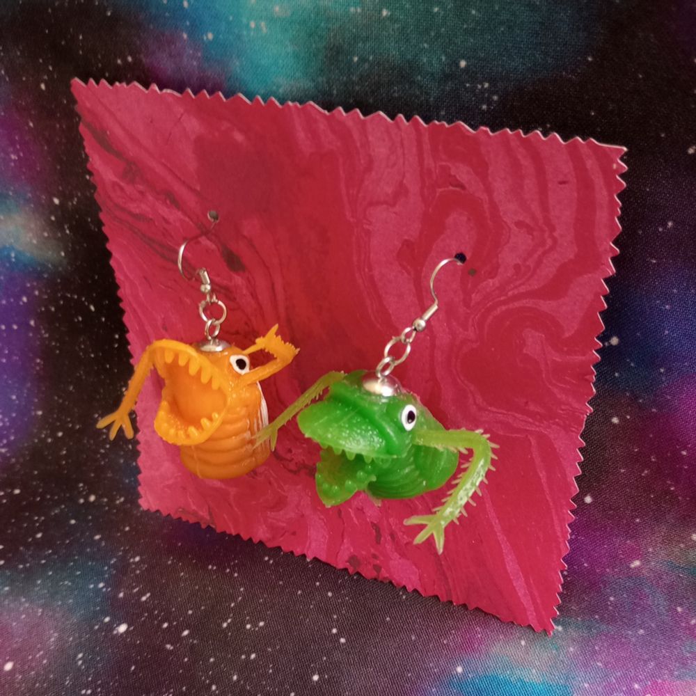 Here's a lovely photo of my monster finger puppet earrings. There's a vintage yellow puppet and a green puppet. They're the sort of finger puppets you could win at the arcade back in the 80s or early 90s. They're dangling from a swirly red card.