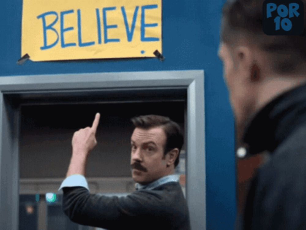 a man pointing to a sign that says believe