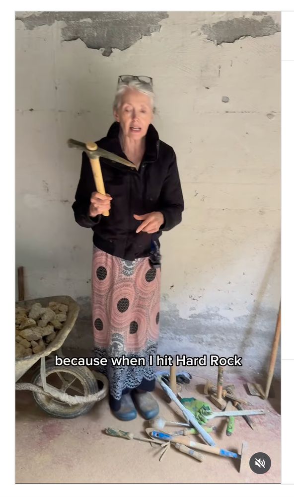 Image of a woman with white hair, reading glasses on her head, wearing a black sweater and pink skirt, holding a pickaxe, with the text, "because when I hit hard rock" from an instagram video by @tatty_macleod

The video is entitled: "Sometimes I do just wish she’d take up knitting. “GRAFTING, IT’S CALLED GRAFTING”"
