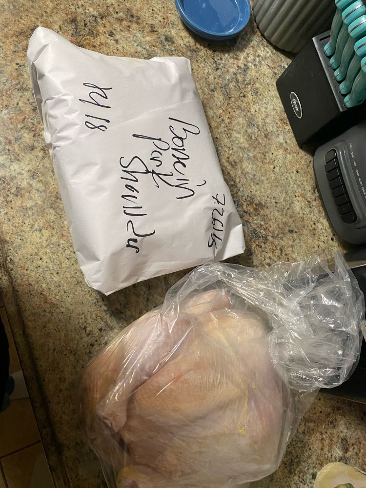 Two pieces of meat on a counter. One is a wrapped pork shoulder, the other is a whole chicken