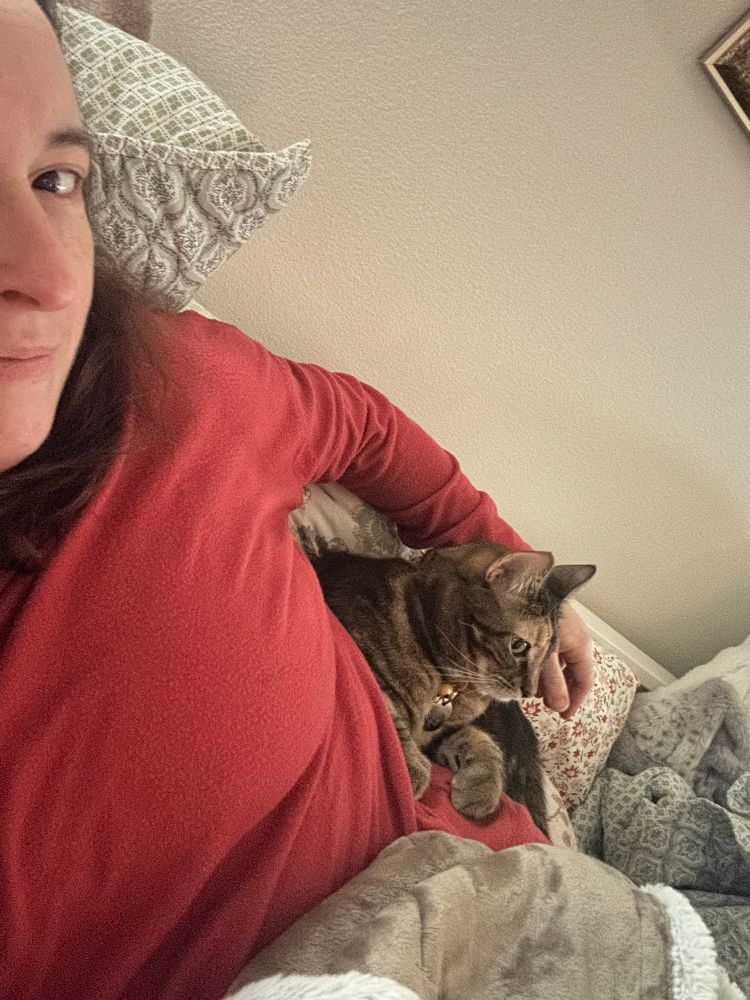 A woman in a red sweater lying down with a cat on her lap