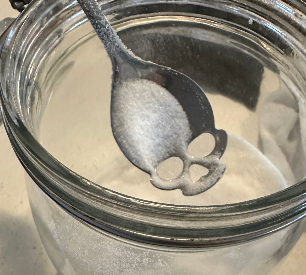 A skull shaped spoon in a jar of sugar. 