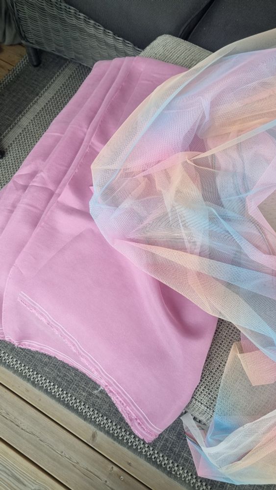 A folded load of pink fabric, with a pastel rainbow-esque soft tulle (pale pink, yellow and blue in wide, gradient stripes) next to it. 