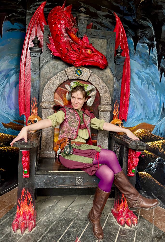photo of me in a jester/faun inspired renaissance faire costume sitting in a dragon throne at bristol renfaire
